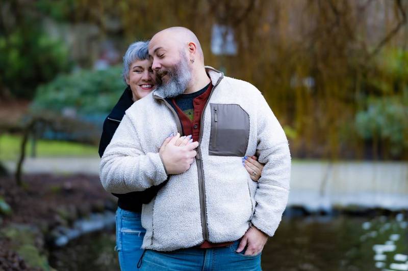 Couple hugging by a pond, both laughing