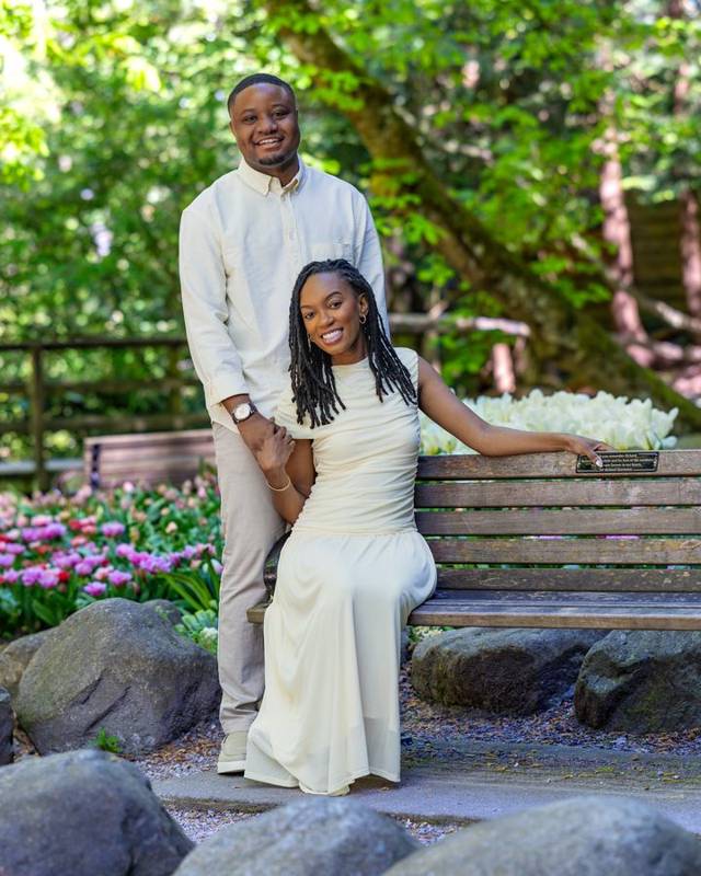 She sits on a garden bench as he stands behind her