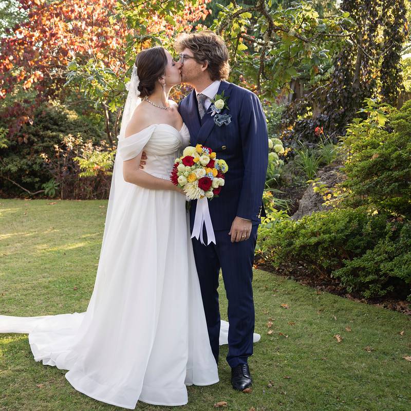 Bride and groom kissing in a garden with autumn colour, bouquet in hand